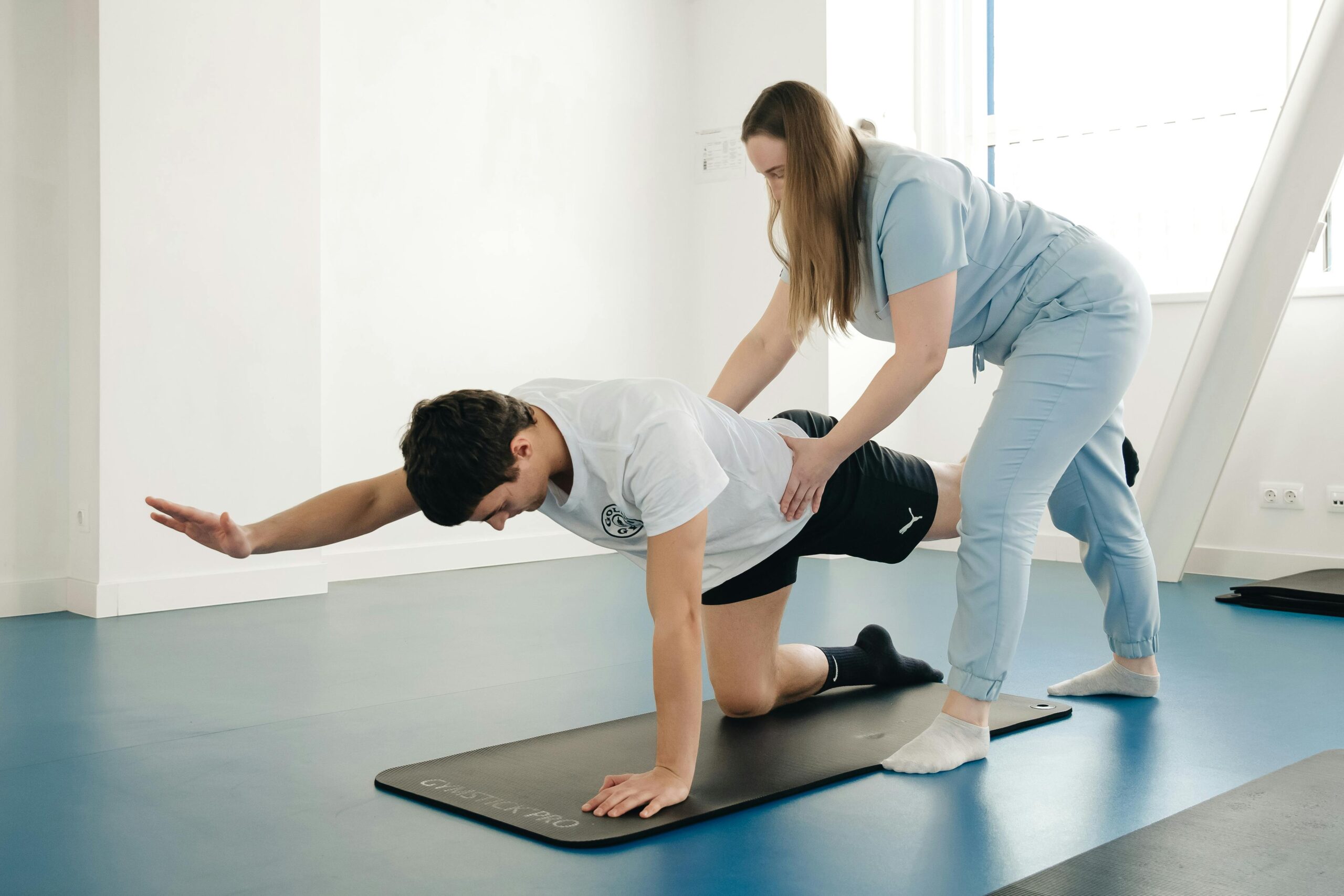 A physiotherapist guides a patient's exercise on a mat in a Vilnius gym.